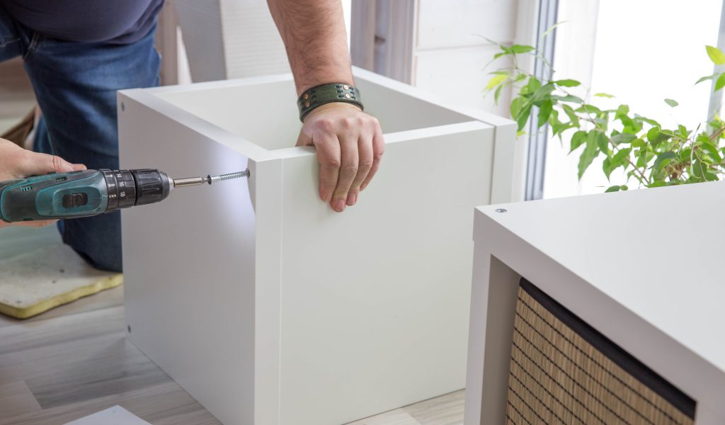 A man assembling purchased furniture in a beautiful room with a large window. Concept of DIY or furniture assembly services